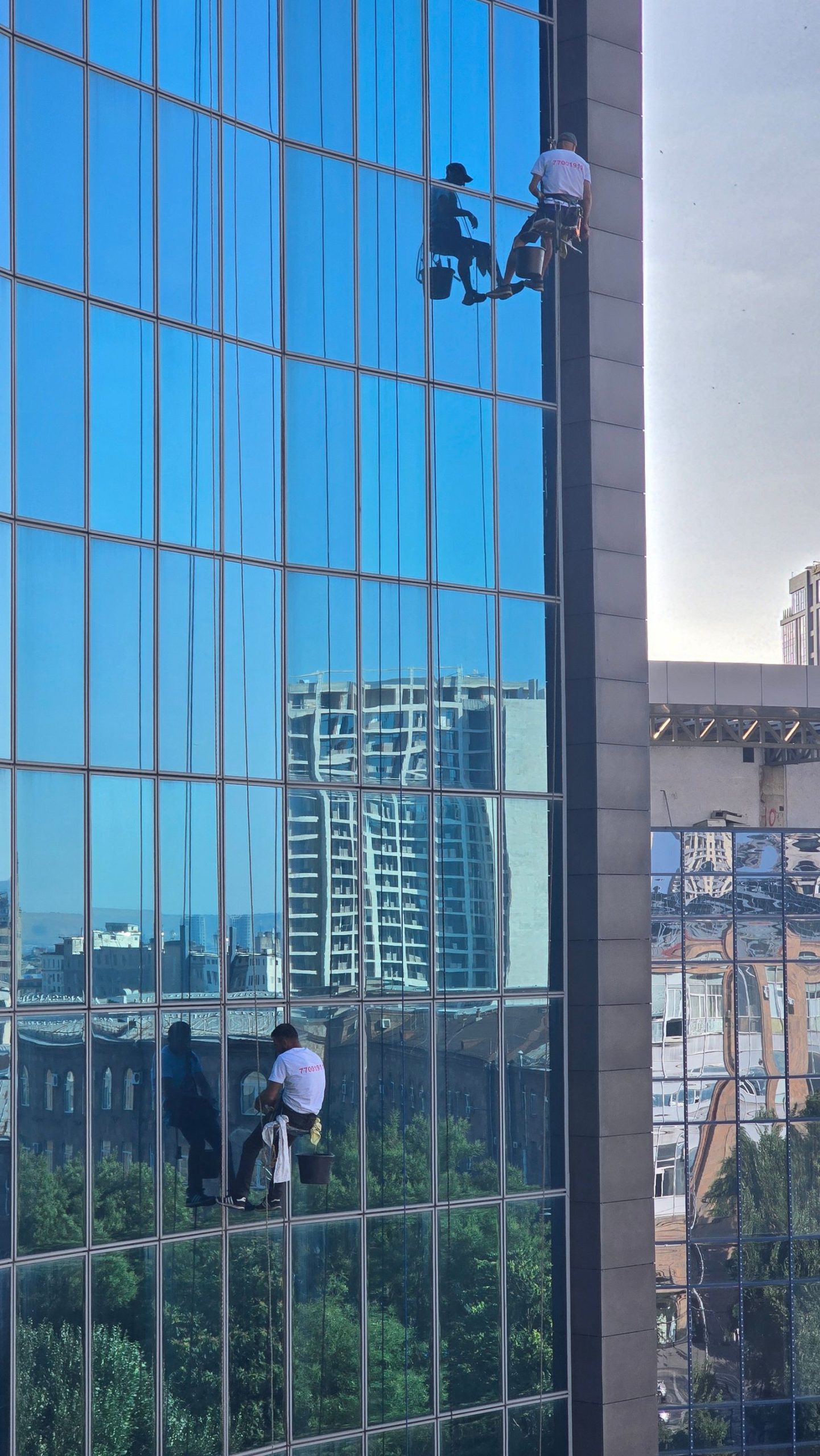 Window cleaners in harnesses working on a reflective high-rise