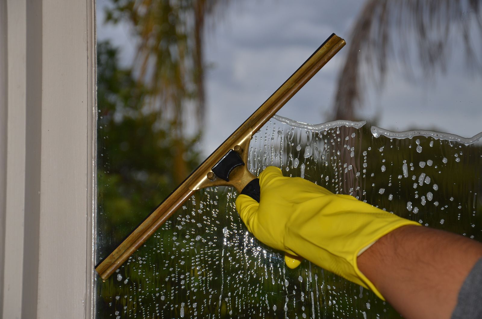 Gloved hand pulling a squeegee across a wet window pane